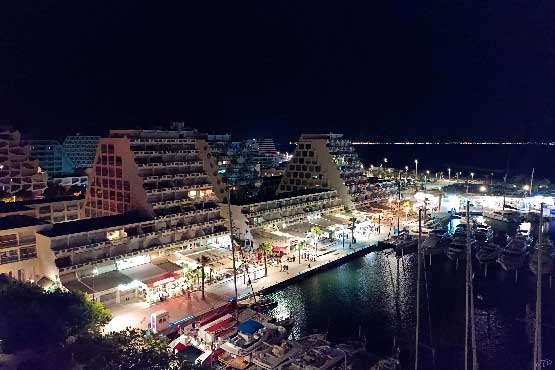 Photo aérienne du port et des commerces de la Grande Motte, station balnéaire de l'Hérault, de nuit